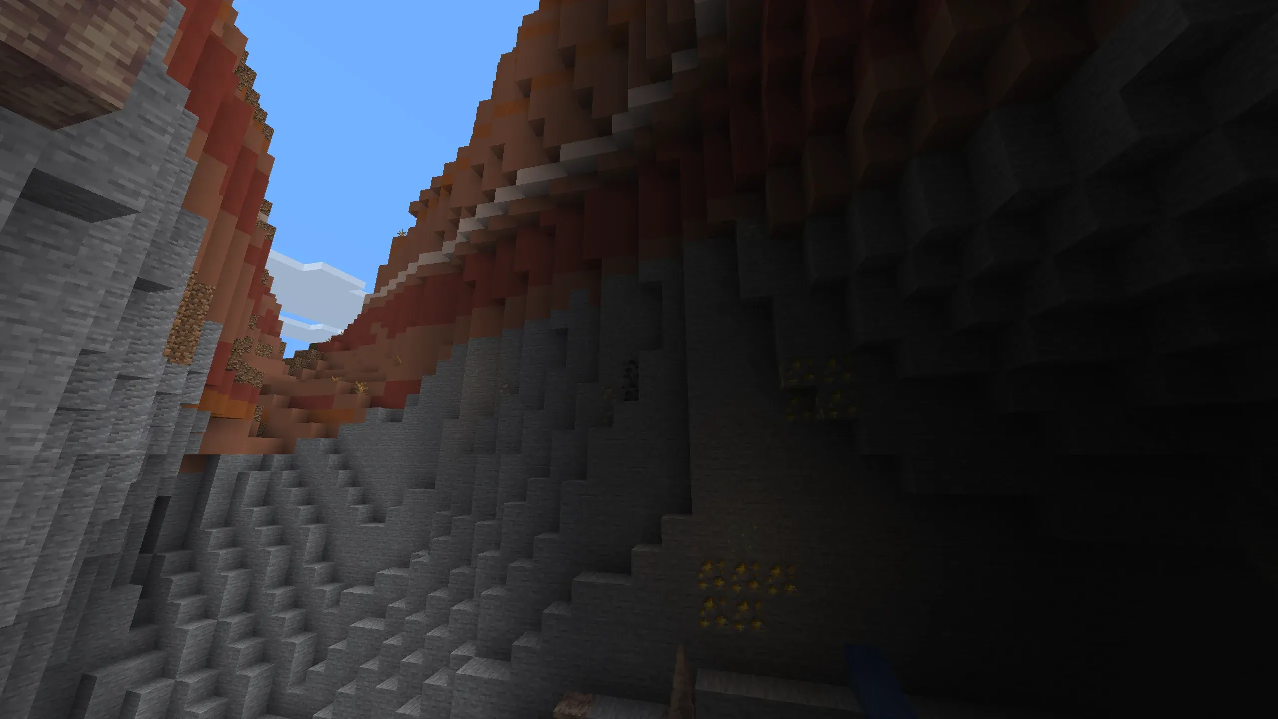 Minecraft Badlands canyon interior with towering layered terracotta cliffs, exposed gold ore, and dramatic low-angle view under blue sky