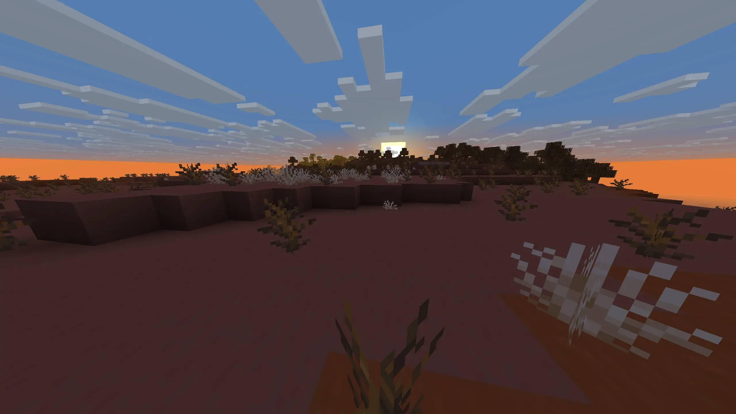 Minecraft Badlands at sunset with vibrant orange sky, setting sun, reddish desert terrain, and scattered dead bushes