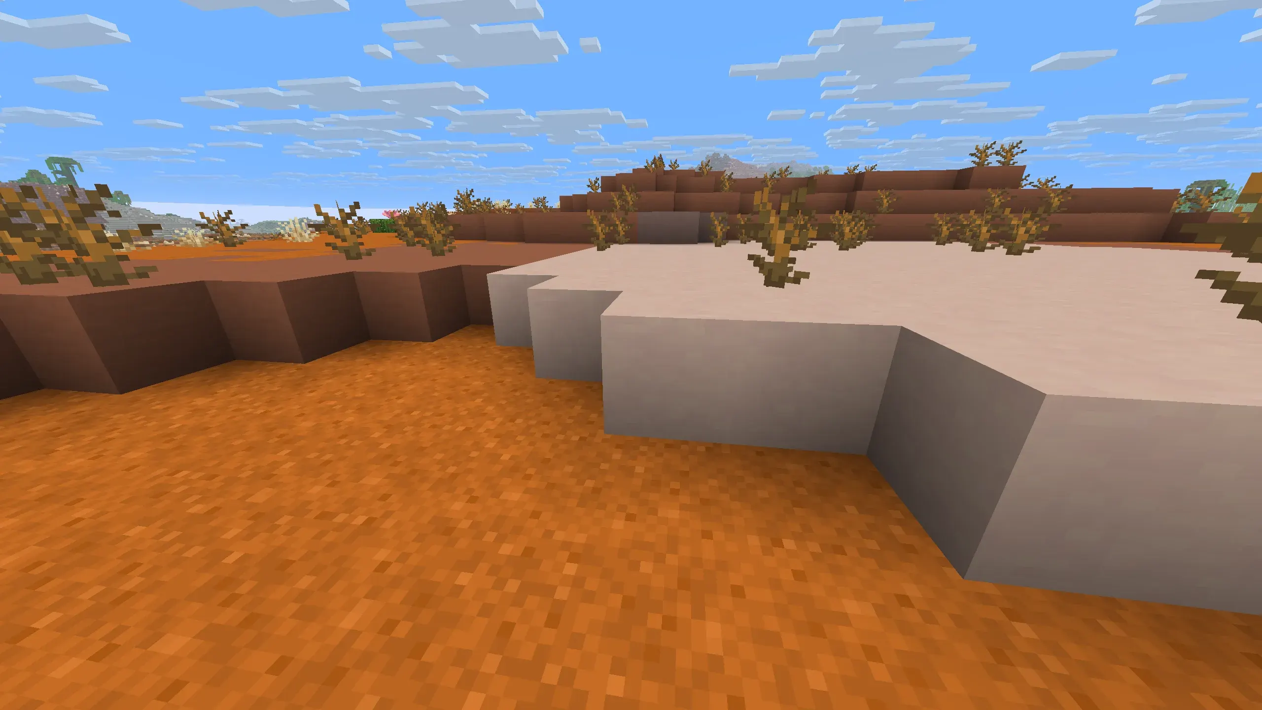 Minecraft desert badlands landscape with orange sand, terracotta cliffs, dead bushes, and a large light-colored sandstone platform under a bright blue sky
